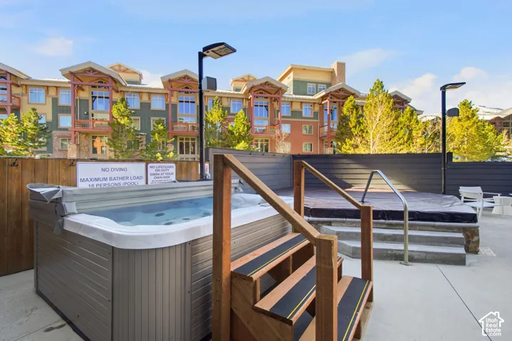 Outdoor spa area featuring a hot tub with wood-finish cabinet, tiered wooden entry steps, concrete hardscaping, and privacy fencing