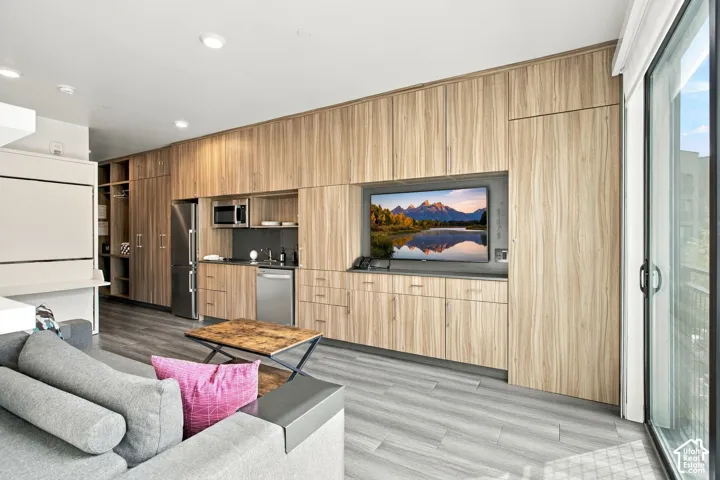 Floor-to-ceiling wood-finish cabinetry, stainless steel appliances, wood-finish flooring, recessed lighting, and a sliding glass door