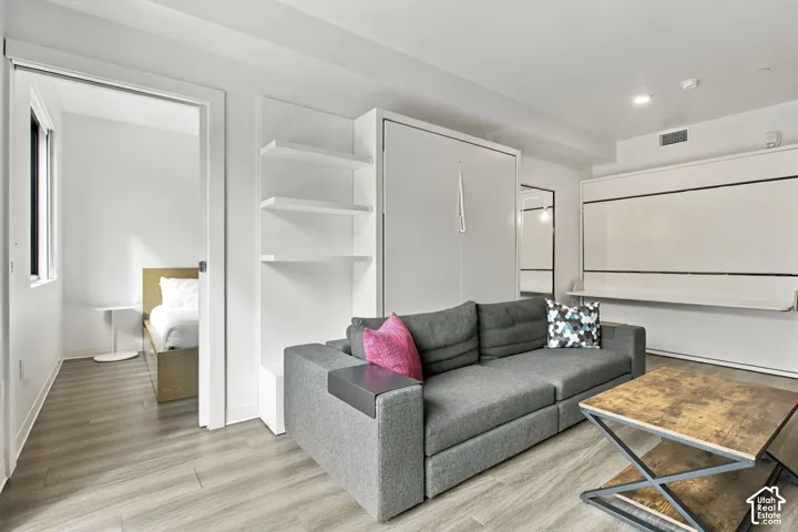 Interior space featuring wood-finish flooring, white built-in wall cabinetry, and a retractable wall-mounted panel system