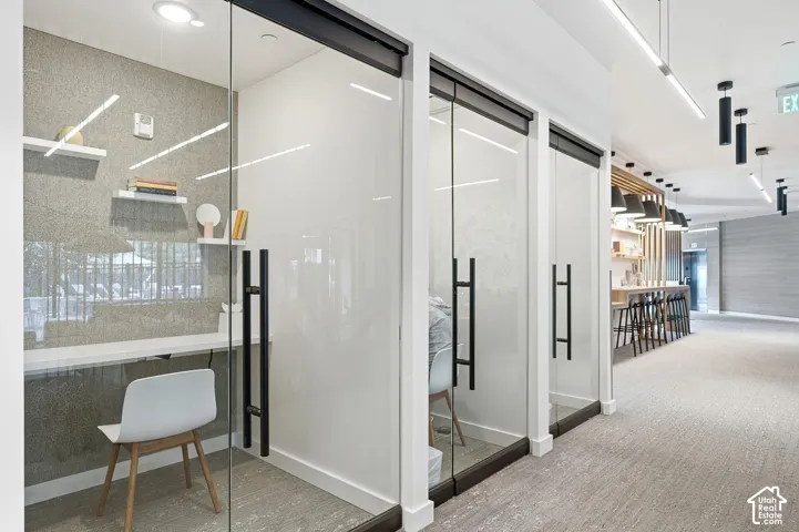 Private workspaces featuring glass partitions with matte black hardware, built-in shelving, integrated desk surfaces, and linear recessed lighting