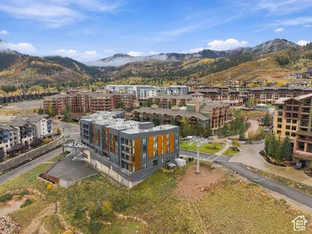 Multi-story structure featuring a combination of dark gray paneling and wood-finish siding, private balconies, and a mountain backdrop
