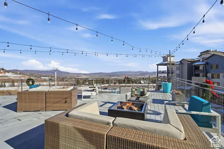 Expansive rooftop terrace featuring concrete flooring, metal cable railing, overhead string lighting, and panoramic mountain scenery