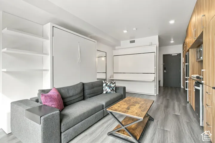 Built-in white wall cabinetry, wood-finish flooring, recessed lighting, and a linear kitchen layout with warm-toned cabinetry