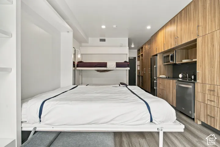 Kitchenette featuring wood-finish cabinetry, stainless steel appliances, built-in storage, and wood-finish flooring