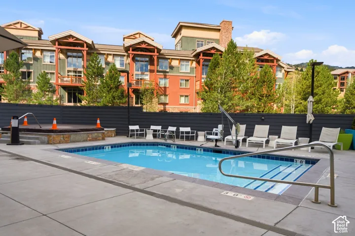 Outdoor swimming pool with concrete decking, stone-base hot tub, and metal safety railings