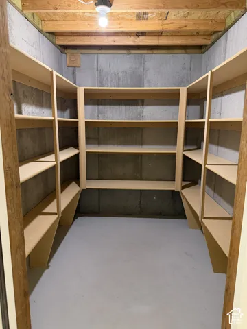 U-shaped configuration of built-in shelving, concrete wall construction, and exposed wood ceiling joists