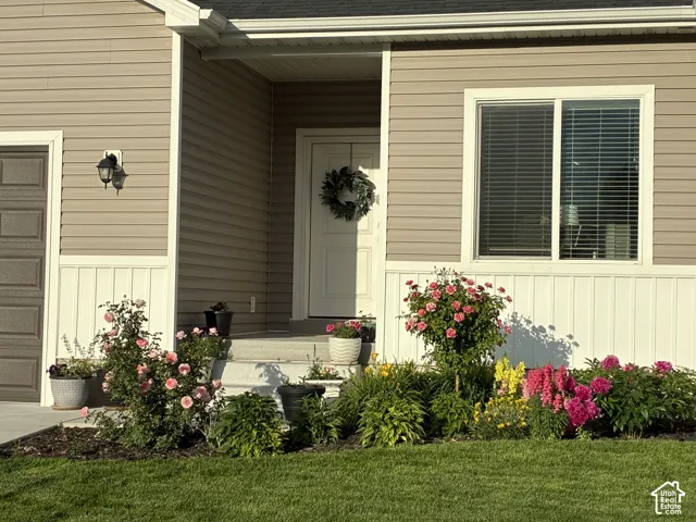 Exterior featuring horizontal vinyl siding, white board-and-batten wainscoting, a covered concrete entry, and established foundation landscaping