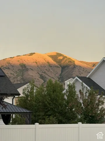 Mountain backdrop featuring large-scale residential rooftops and a solid white privacy fence