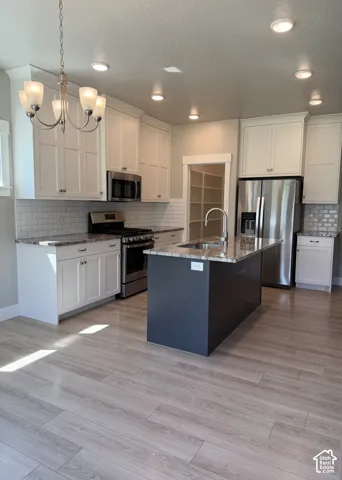 Kitchen featuring white cabinetry, stone-finish countertops, subway tile backsplash, center island with built-in sink, and wood-finish flooring