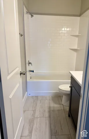 Bathroom featuring a white bathtub, white subway tile surround with integrated shelving, dark-finish cabinetry, and stone-look tile flooring