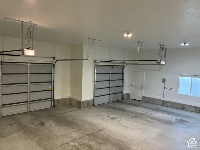 Multi-vehicle garage with dual overhead doors, concrete flooring, interior pedestrian access door, and recessed lighting