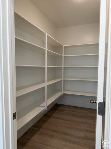 Walk-in pantry featuring multi-level built-in white shelving and wood-finish flooring