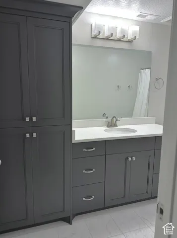 Full-height cabinetry, vanity with countertop, undermount sink, multi-light fixture, and tile flooring