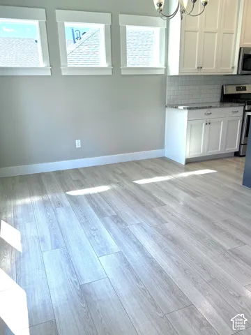 Kitchen featuring wood-finish flooring, white cabinetry, a subway tile backsplash, and three windows with trim detail