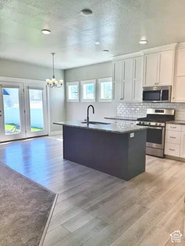 Kitchen featuring white cabinetry, a center island with a dark base and stone countertop, stainless steel appliances, light-toned wood-finish flooring, and subway tile backsplash