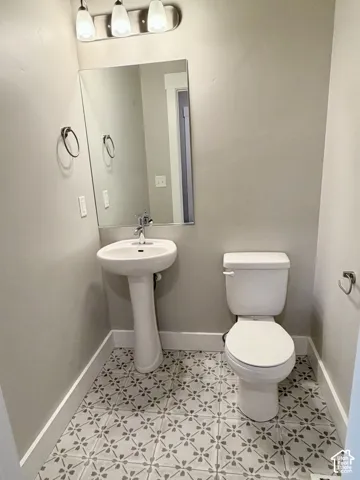 Pedestal sink with chrome faucet, large vanity mirror, patterned tile flooring, and three-light overhead fixture