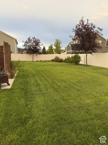 Expansive backyard featuring a level lawn, solid vinyl fencing, mature trees, and a concrete patio