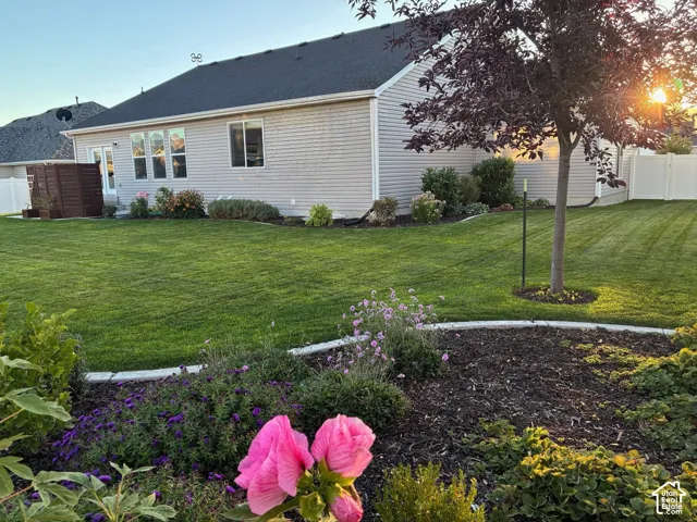 Rear exterior featuring vinyl siding, expansive lawn, stone-edged garden beds, and white vinyl privacy fencing