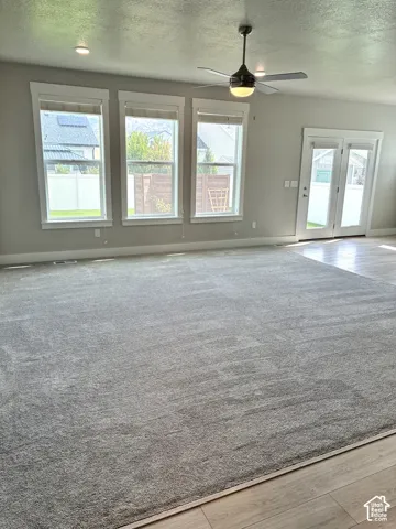 Spacious room featuring neutral carpeting, recessed lighting, a modern ceiling fan, three paneled windows with roller shades, and double glass-paned doors