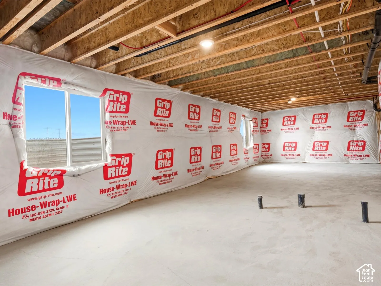Unfinished lower level featuring concrete flooring, exposed wood ceiling joists, protective wall wrap, and multiple egress windows