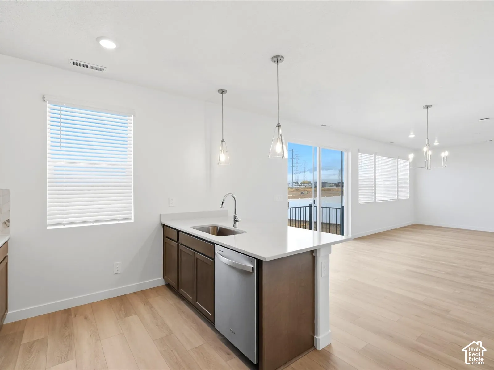 **DISCLAIMER** Interior package may vary. Kitchen featuring a peninsula with a composite countertop and stainless steel undermount sink, wood-finish cabinetry, stainless steel dishwasher, pendant lighting, and wood-finish flooring