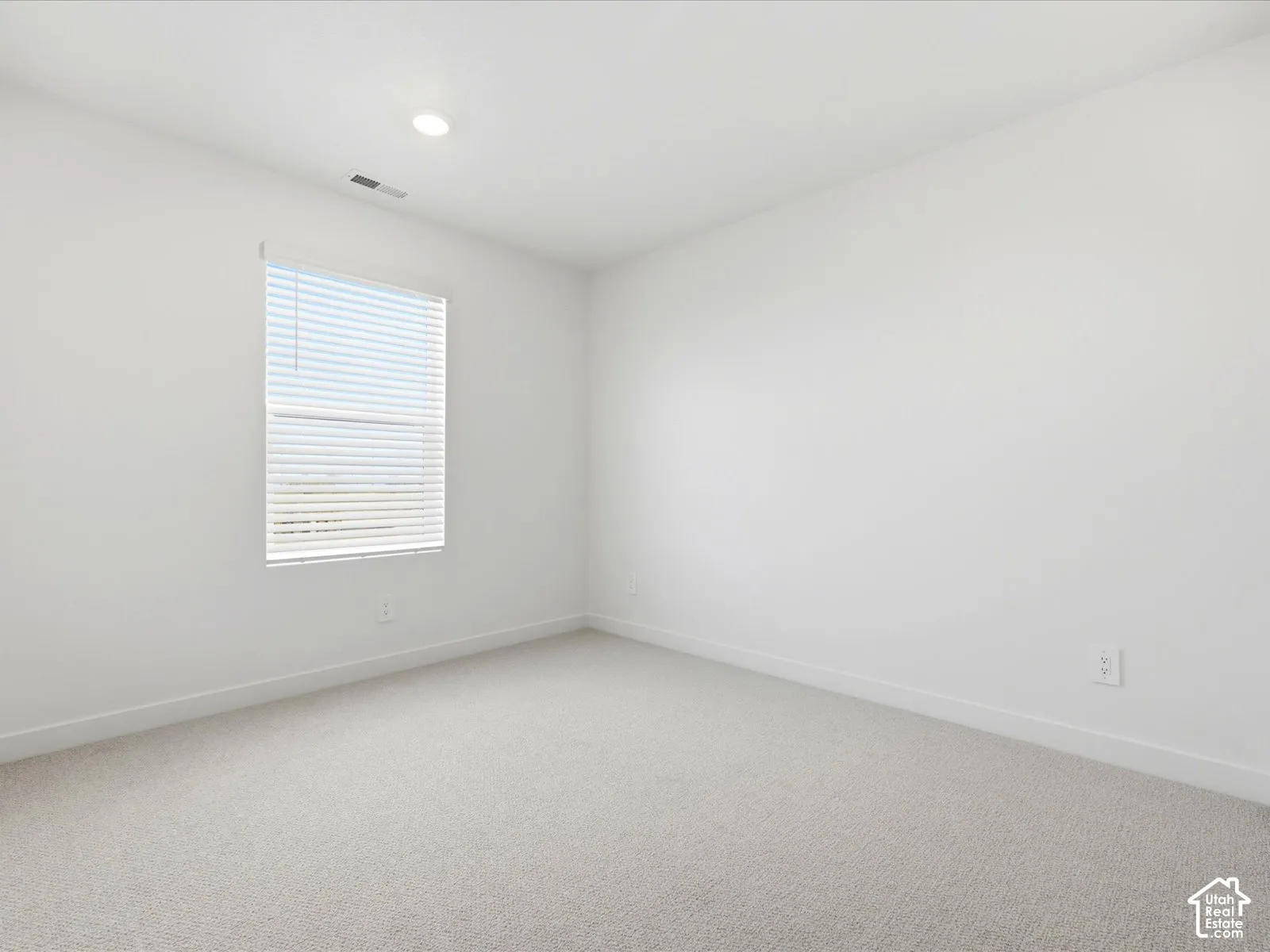 Neutral interior space featuring high-pile carpeting, neutral wall paint, and a window with horizontal blinds, illuminated by recessed lighting