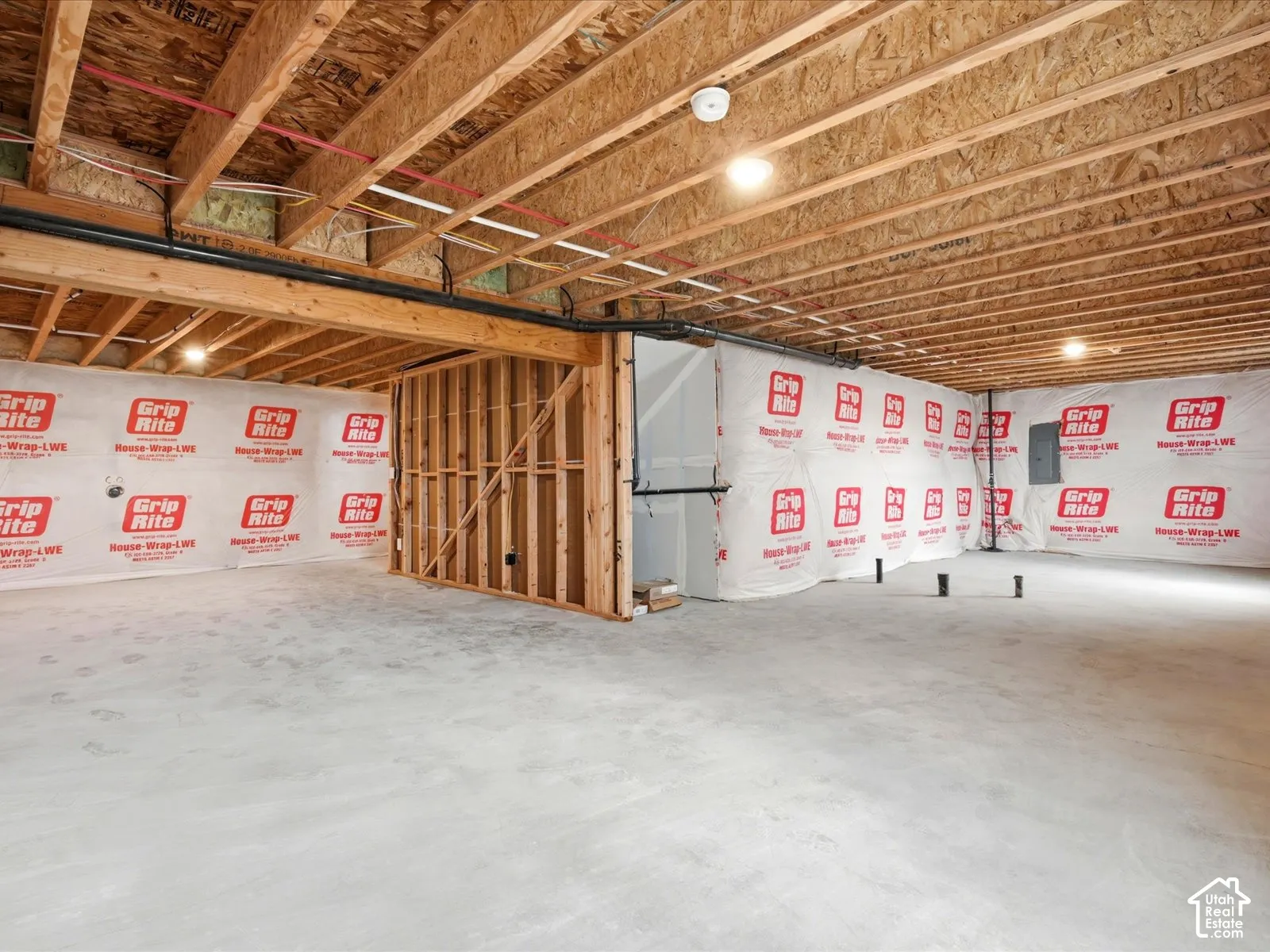 Unfinished lower level featuring concrete flooring, exposed wood joist ceilings, and protective house wrap on perimeter walls