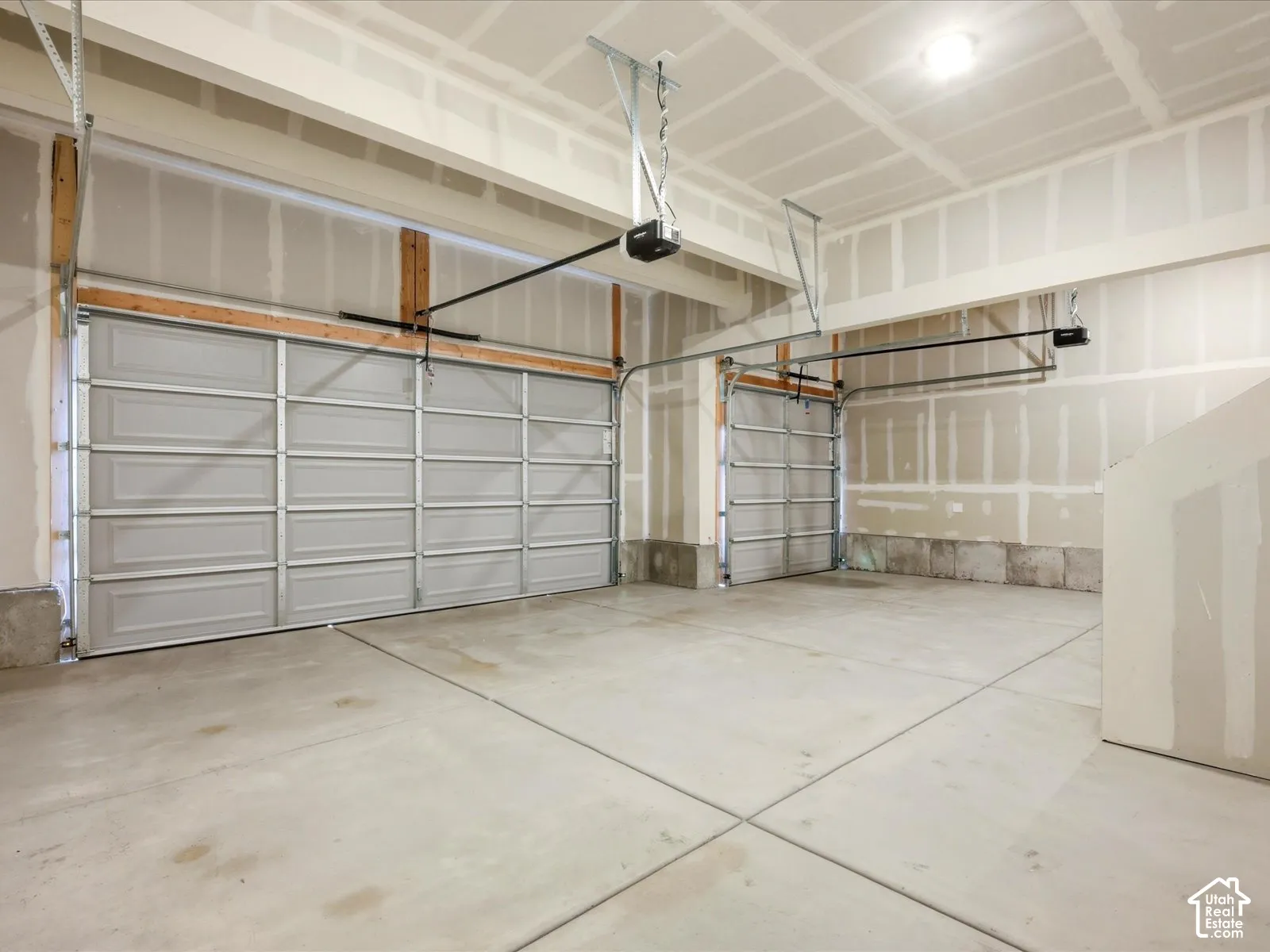 Three-car garage featuring finished concrete flooring, dual automatic door openers, and exposed structural beams