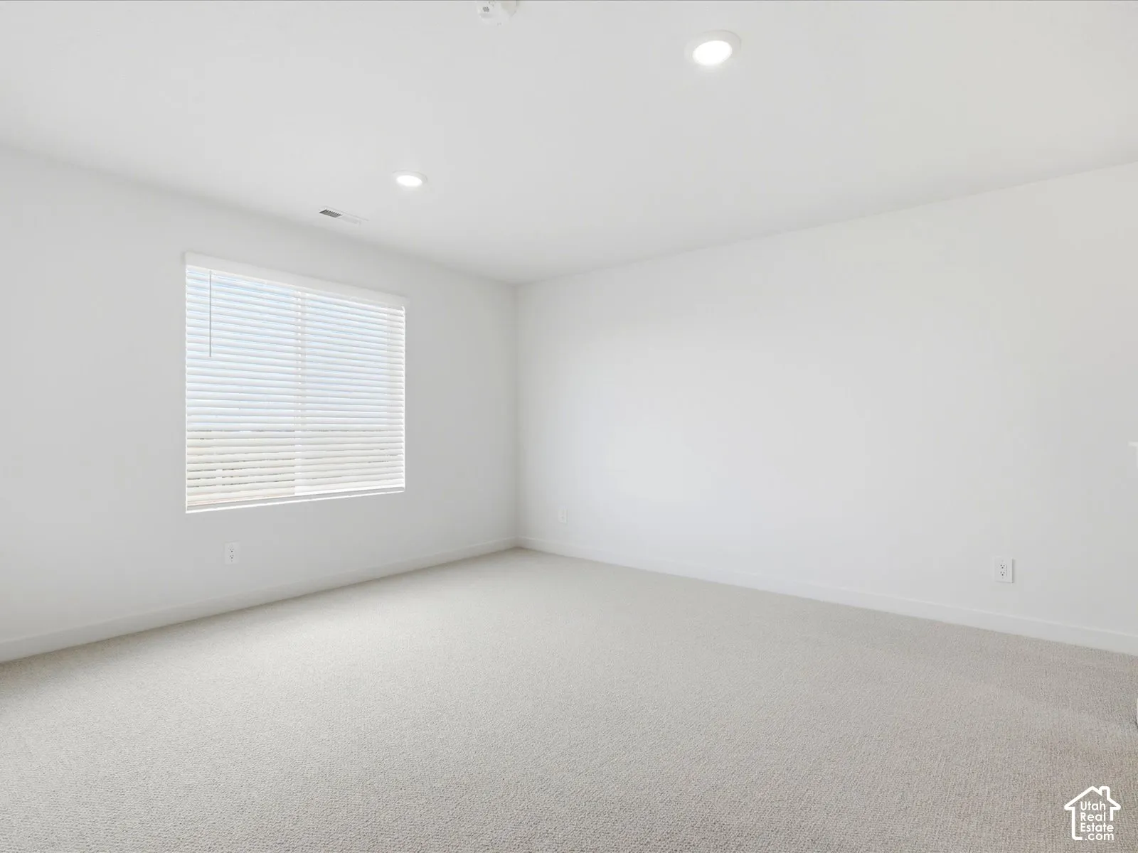 Neutral interior space featuring high-pile wall-to-wall carpeting, recessed ceiling lighting, and a single window with integrated horizontal blinds