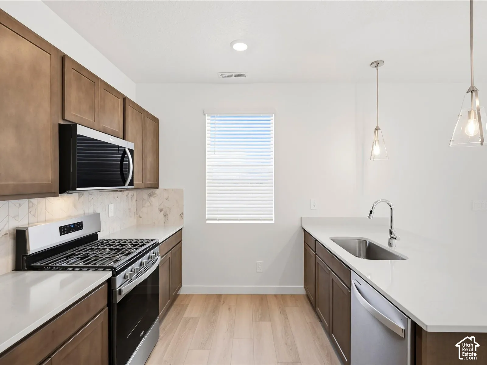 **DISCLAIMER** Interior package may vary. Kitchen featuring wood-finish cabinetry, quartz countertops, patterned tile backsplash, stainless steel appliances, and dual pendant lighting