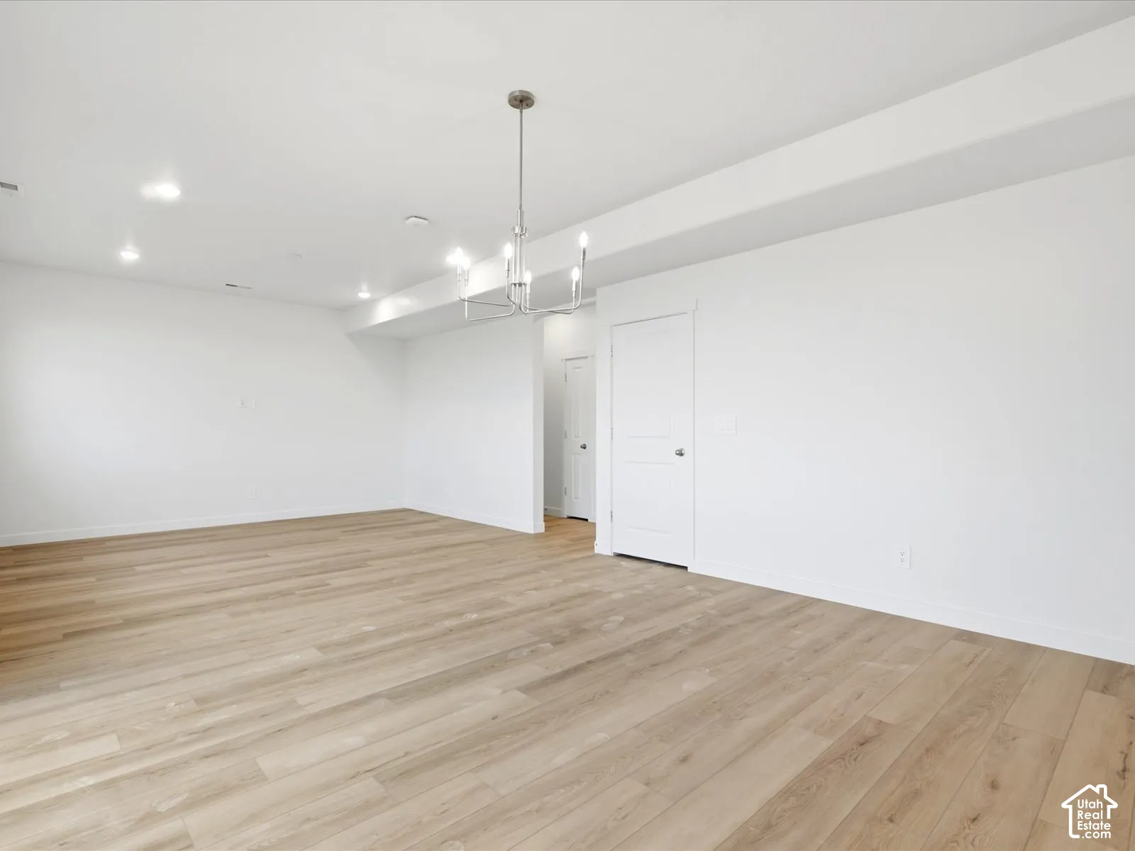 **DISCLAIMER** Interior package may vary. Interior space featuring wood-finish flooring, recessed lighting, a multi-arm metallic chandelier, and a panel door