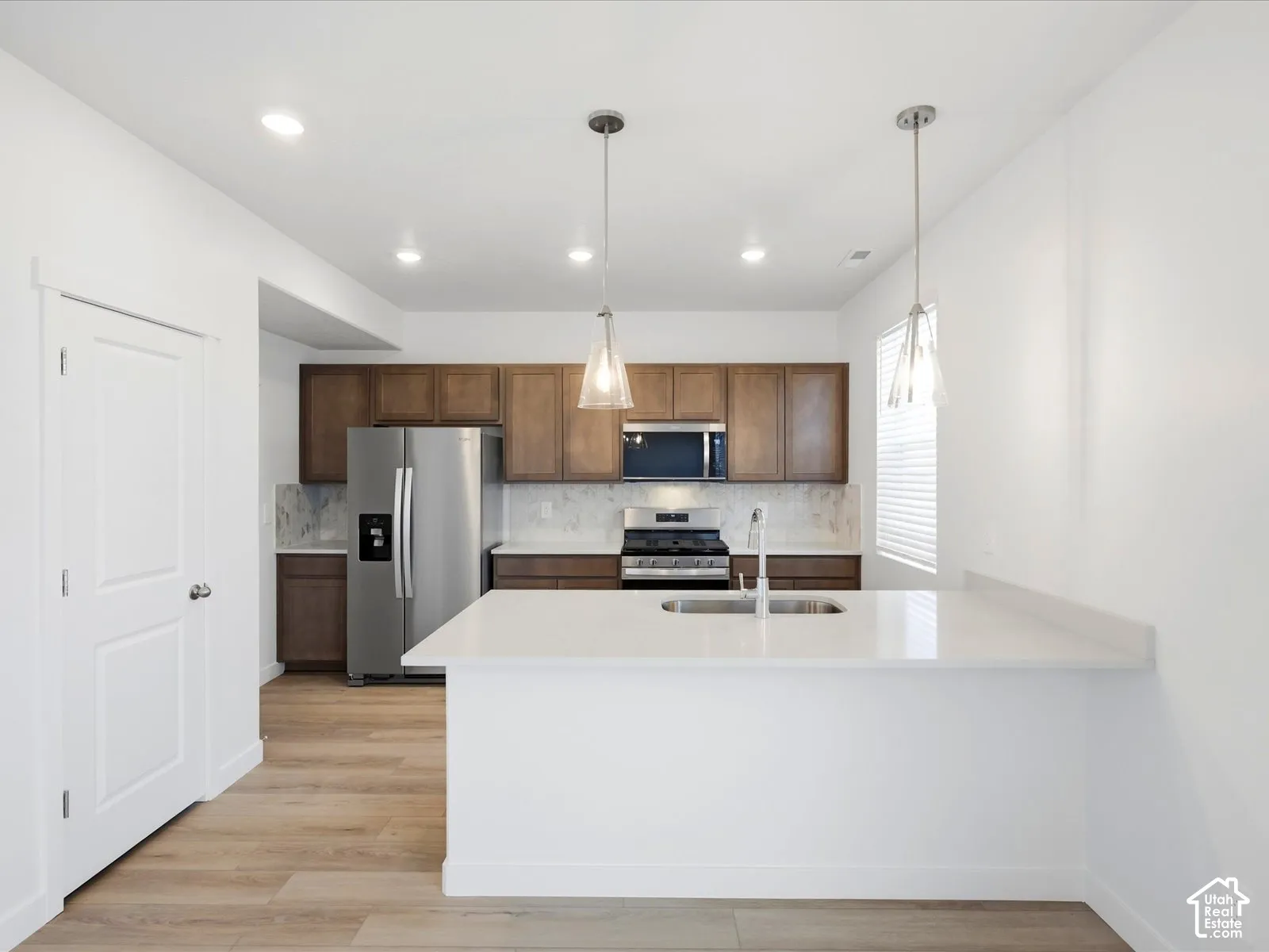 **DISCLAIMER** Interior package may vary. Kitchen featuring wood-finish cabinetry, stone-surface countertops, stainless steel appliances, a peninsula with an undermount sink, and two glass pendant lights
