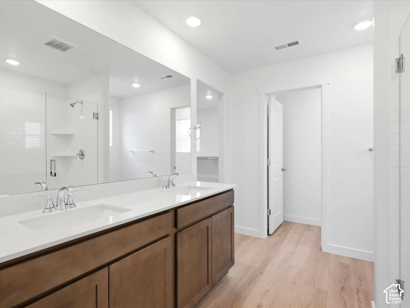 **DISCLAIMER** Interior package may vary. Double vanity featuring a light-toned countertop with integrated dual sinks, dark wood cabinetry, a full-width wall mirror, and wood-finish flooring