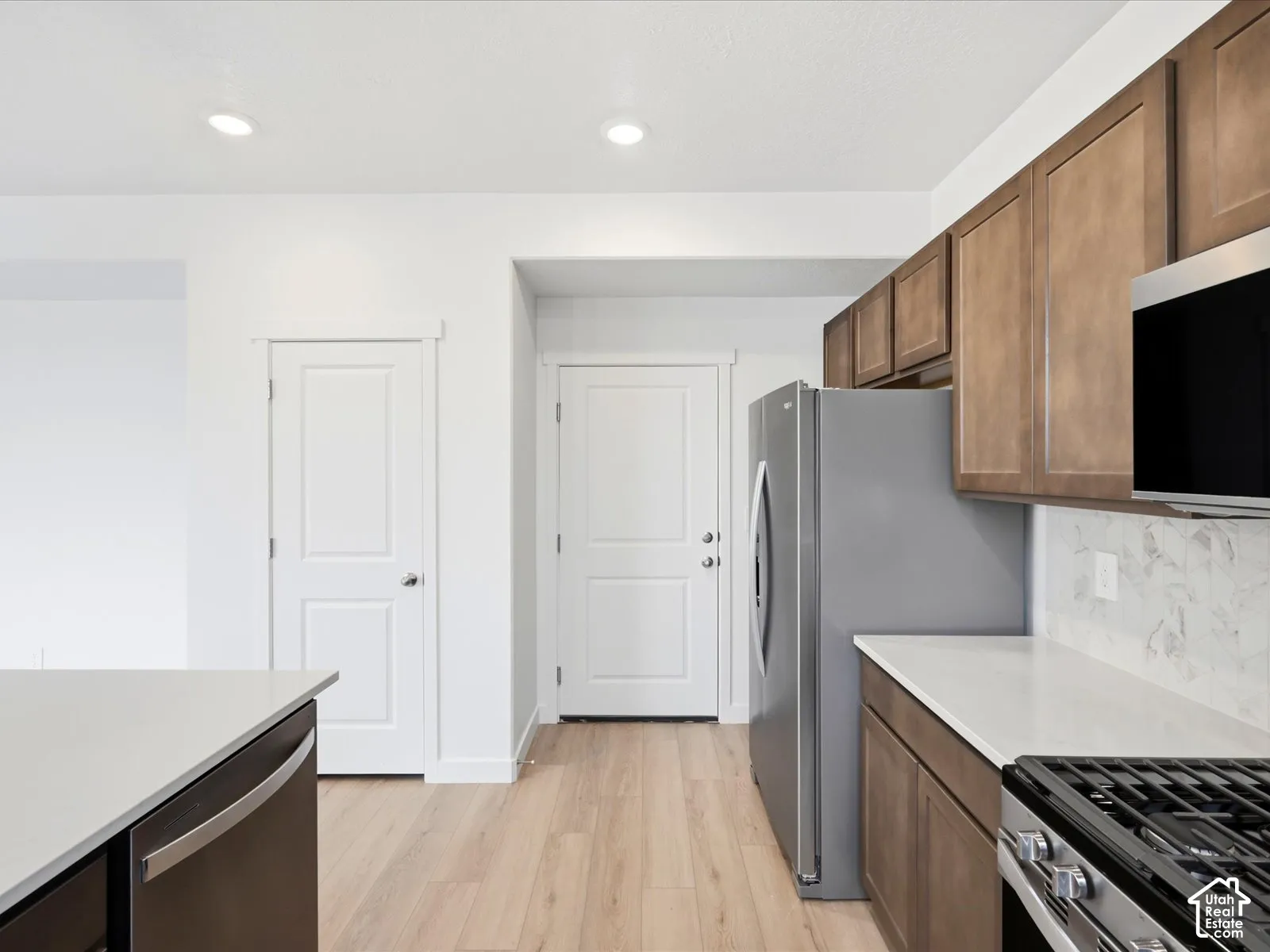 **DISCLAIMER** Interior package may vary. Kitchen featuring stained wood cabinetry, stone-finish countertops, tile backsplash, stainless steel appliances, and wood-finish flooring