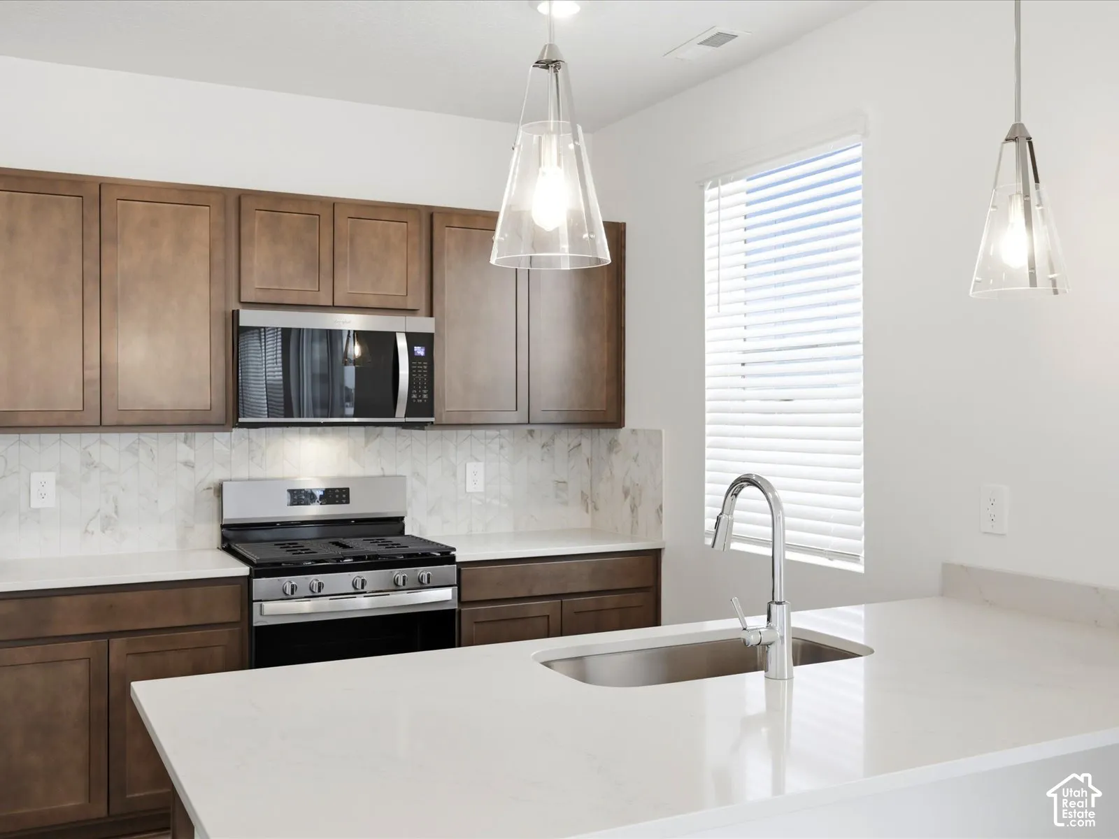 **DISCLAIMER** Interior package may vary. Kitchen featuring shaker-style cabinetry, quartz countertops, a patterned tile backsplash, stainless steel gas range with built-in microwave, and dual glass pendant light fixtures