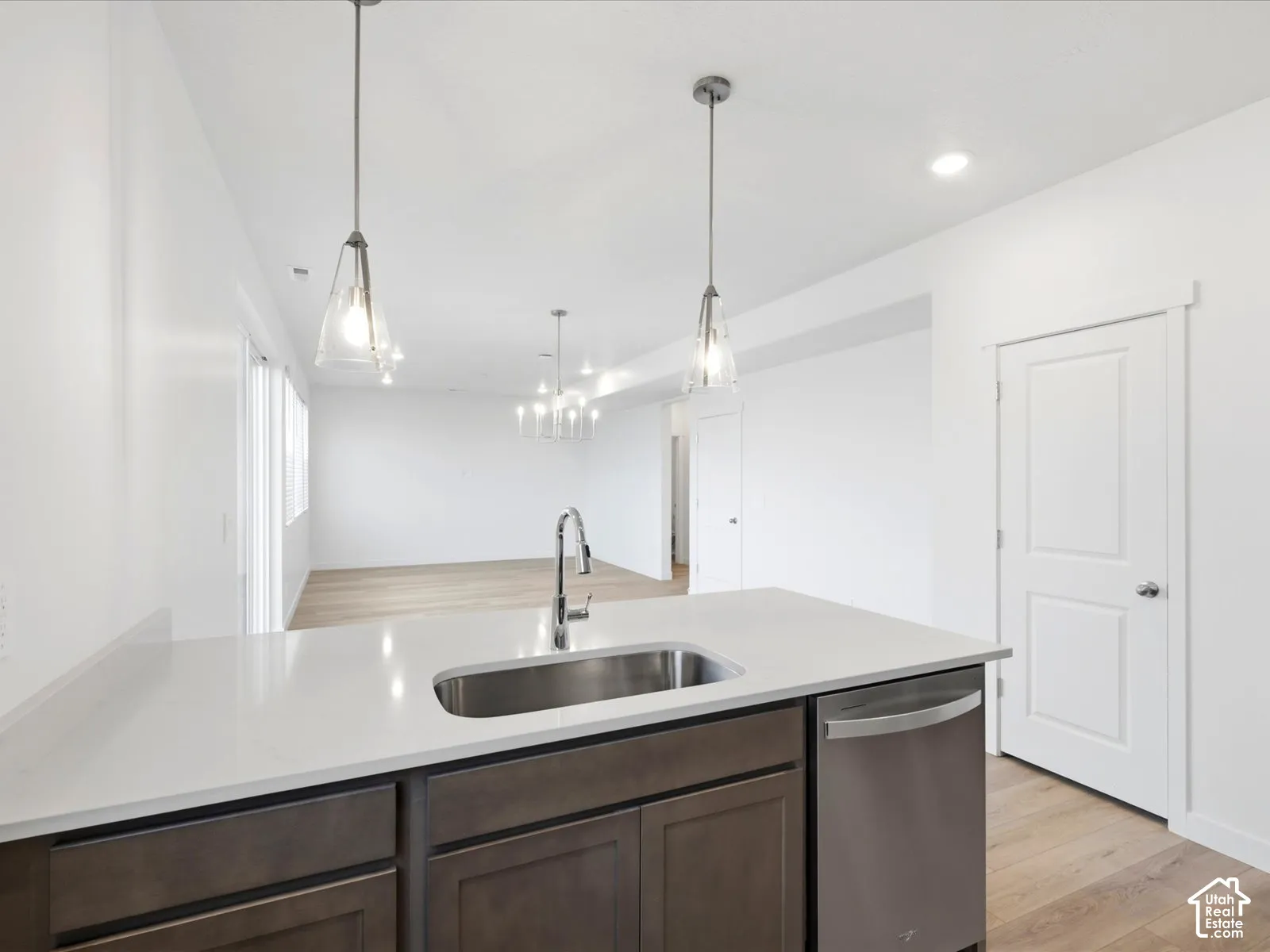 **DISCLAIMER** Interior package may vary. Kitchen island featuring a solid-surface countertop, stainless steel undermount sink with a gooseneck faucet, shaker-style cabinetry, stainless steel dishwasher, and dual glass pendant lighting