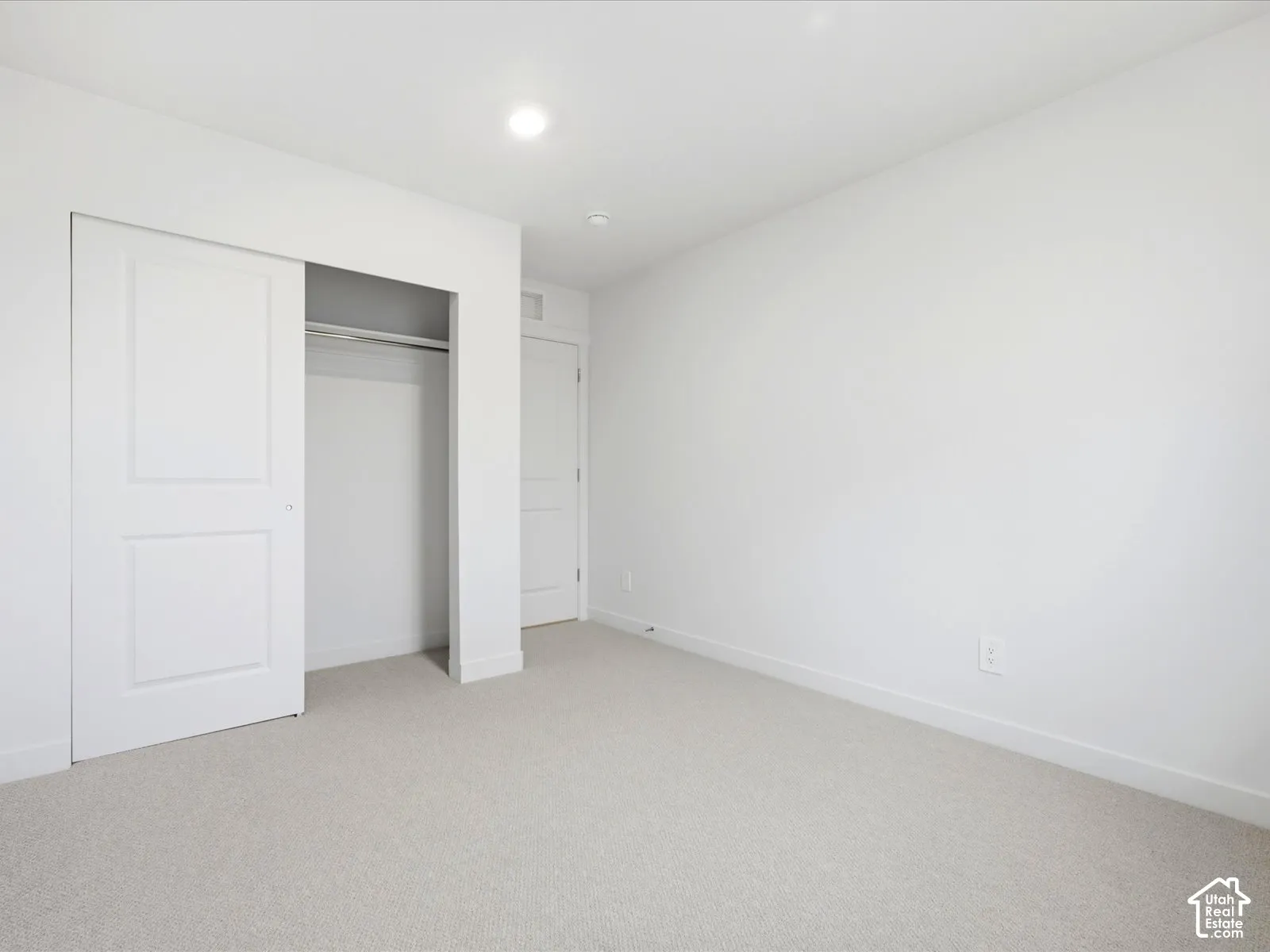 Neutral-toned carpeted flooring, recessed ceiling lighting, and a reach-in closet featuring a sliding paneled door
