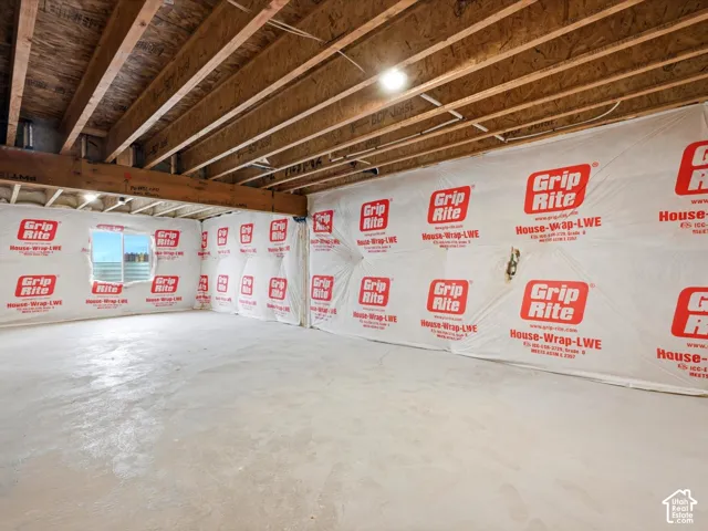Unfinished interior space featuring exposed wooden floor joists, concrete flooring, and a window with a mountain backdrop