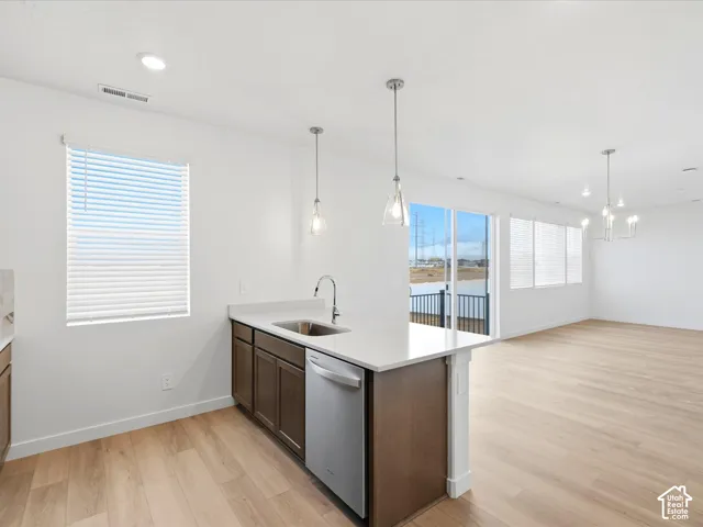 **DISCLAIMER** Interior package may vary. Kitchen featuring a peninsula with a composite countertop and stainless steel undermount sink, wood-finish cabinetry, stainless steel dishwasher, pendant lighting, and wood-finish flooring
