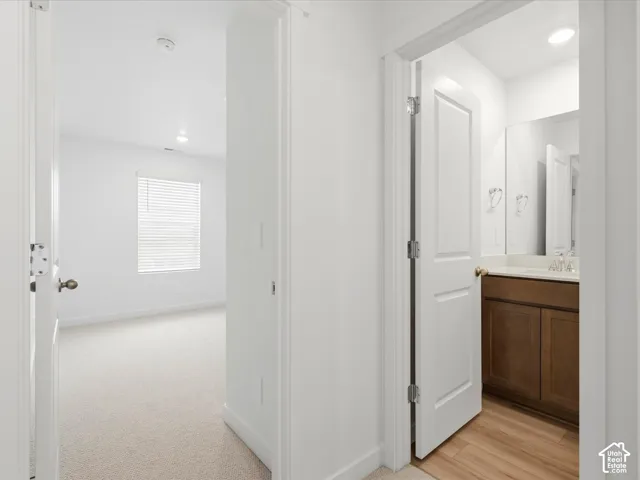 **DISCLAIMER** Interior package may vary. Interior hallway featuring neutral carpeting, recessed ceiling lighting, a bathroom with a wood-finish vanity, light-toned countertop, and rectangular wall mirror