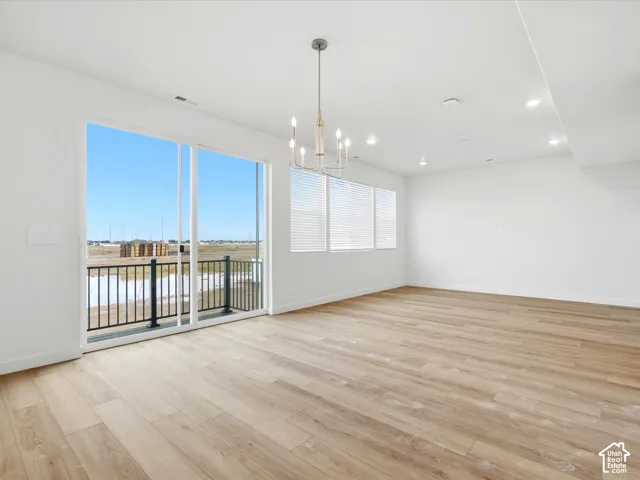 **DISCLAIMER** Interior package may vary. Open-concept interior featuring light wood-finish flooring, sliding glass patio doors, a black metal balcony railing, recessed lighting, and a multi-arm chandelier