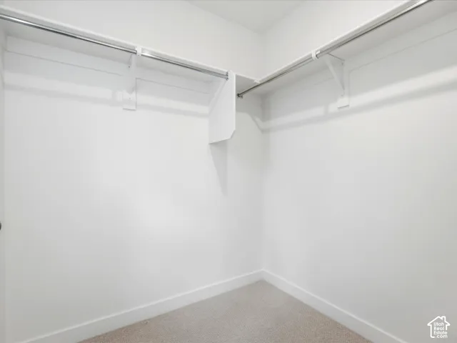 Walk-in closet featuring white walls, neutral carpeting, and built-in white shelving with integrated metal rods