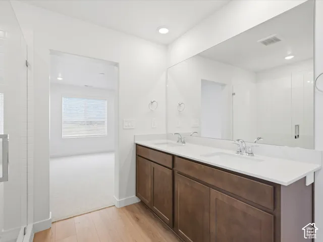 **DISCLAIMER** Interior package may vary. Dual-sink vanity with a solid-surface countertop, dark wood-finish cabinetry, a full-width wall mirror, and a glass-enclosed shower