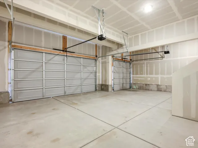 Three-car garage featuring finished concrete flooring, dual automatic door openers, and exposed structural beams