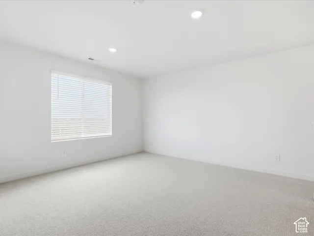 Neutral interior space featuring high-pile wall-to-wall carpeting, recessed ceiling lighting, and a single window with integrated horizontal blinds