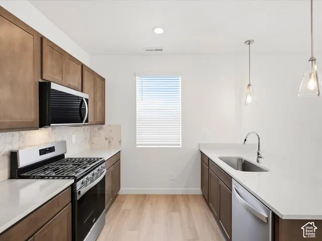 **DISCLAIMER** Interior package may vary. Kitchen featuring wood-finish cabinetry, quartz countertops, patterned tile backsplash, stainless steel appliances, and dual pendant lighting