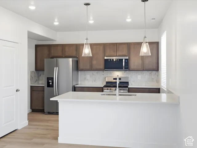**DISCLAIMER** Interior package may vary. Kitchen featuring wood-finish cabinetry, quartz countertops, a stone-tile backsplash, stainless steel appliances, and dual pendant lighting