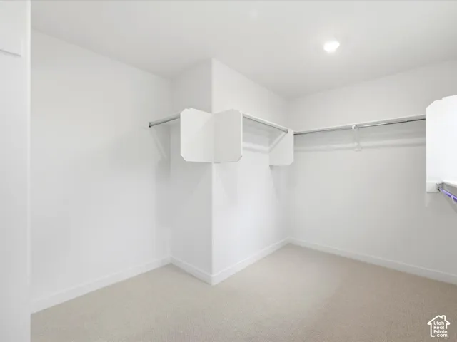 Walk-in closet featuring neutral carpeting, white walls, and built-in white shelving with integrated hanging rods