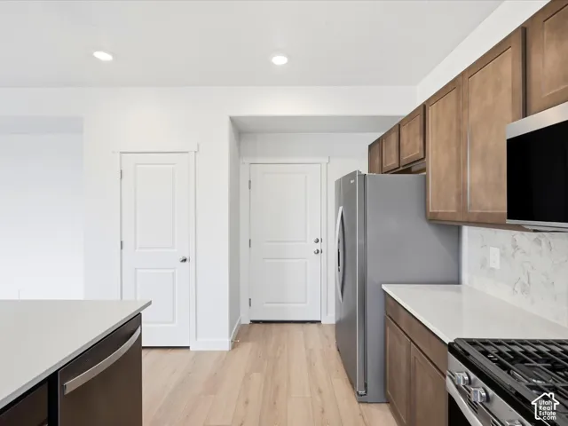 **DISCLAIMER** Interior package may vary. Kitchen featuring stained wood cabinetry, stone-finish countertops, tile backsplash, stainless steel appliances, and wood-finish flooring