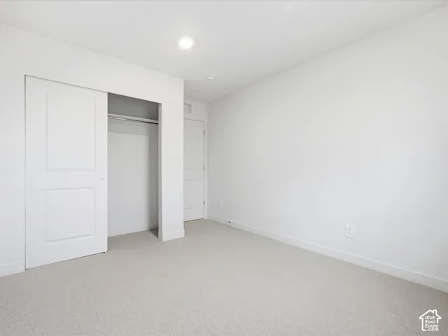 Neutral-toned carpeted flooring, recessed ceiling lighting, and a reach-in closet featuring a sliding paneled door